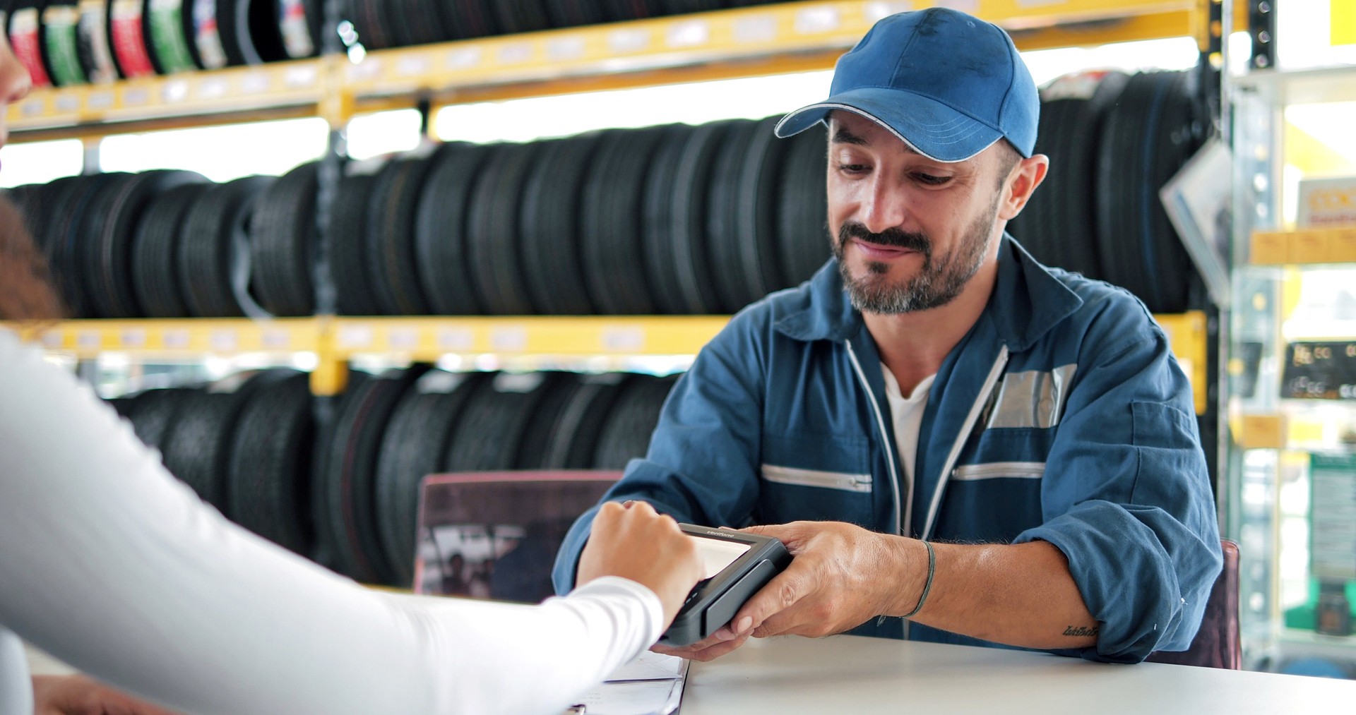 Car mechanic man in blue uniform hold payment terminal for paying with credit card while owner driver customer using credit card touching for pay at vehicle repair shop