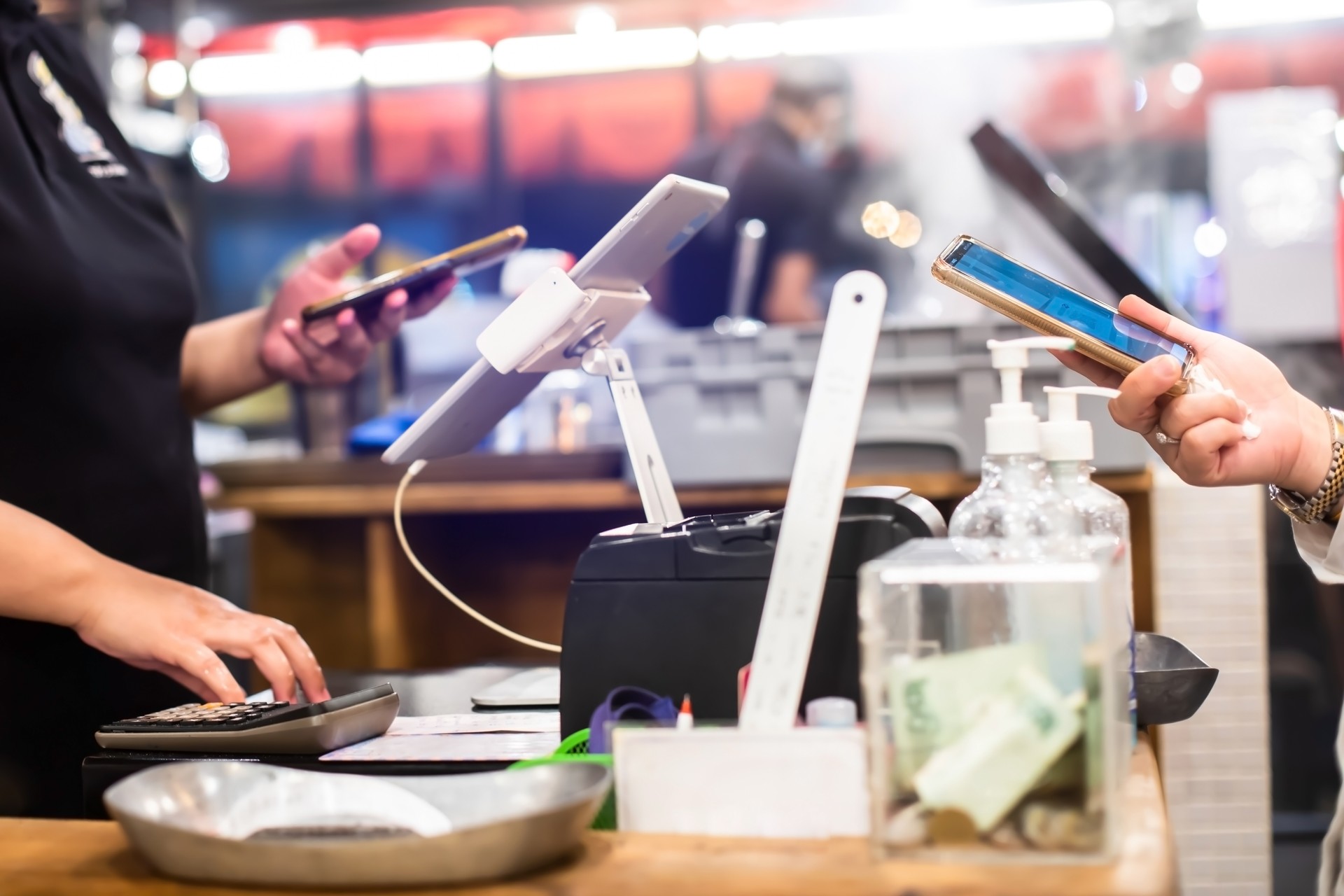 Selective focus to edge of smartphone in hand with blurry the tablet and cashier staff using it to receive orders from customers at counter service.